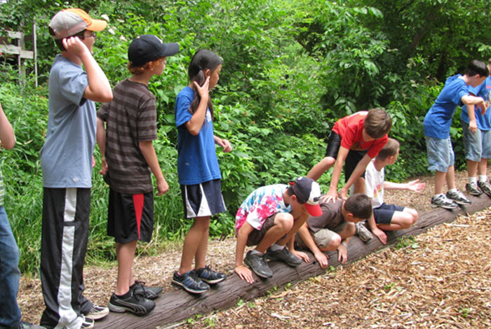 group of kids balancing on tree trunk and play playing Telephone Pole Shuffle